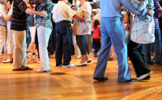 Many happy senior couples in love dancing on wooden dance floor. Focus on right shoe.